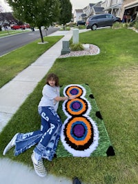 a girl laying on the grass with a colorful rug